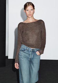 Hnědý pletený svetr se širokým výstřihem, kombinovaný se světle modrými džíny s vysokým pasem a bočními knoflíky. Jednoduchý, ležérní design.