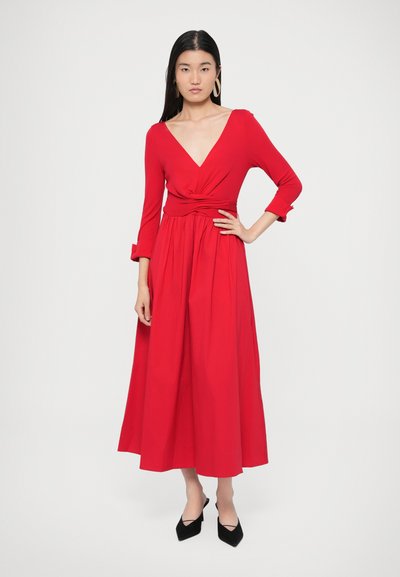 Piros, hosszú ujjú, V-nyakú ruha csomós derékrésszel és lenge szoknyával. Sima anyagból, közép-vádli hosszúságú, fekete hegyes orrú cipővel párosítva.