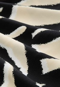 Un tissu avec un fond noir orné de motifs abstraits en beige et blanc à coups de pinceau. Texture douce avec une apparence lisse et fluide.