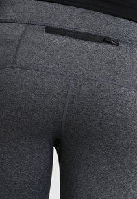 Primo piano di leggings sportivi grigi con vita alta e una piccola tasca con zip orizzontale sul retro.