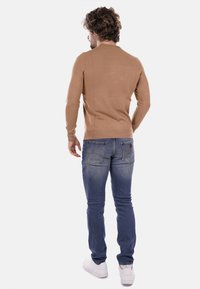 Camicia a maniche lunghe color marrone chiaro con un design aderente. Indossata con jeans in denim blu e sneakers bianche, vista da dietro.
