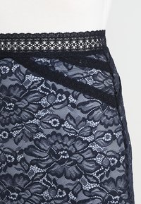Marinblå spetskjol med blommönster, vågig övre kant och lagerdesign med genomskinlig struktur, som framhäver det intrikata detaljarbetet.