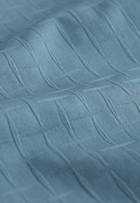 Tissu bleu texturé avec un motif de lignes en relief entrelacées. Le matériau semble doux, avec une finition mate et une légère brillance.