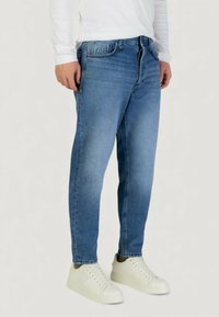 Jeans de mezclilla azul claro con corte recto, diseño de cinco bolsillos y sutiles desvanecimientos. Combinados con zapatillas blancas, mostrando un look limpio.