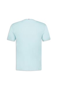 Světle modré tričko s krátkým rukávem vyrobené z bavlny. Má kulatý výstřih a malou nášivku s trojbarevným akcentem na zadní straně krku. Jednoduchý design.