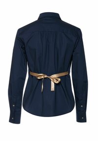 Tengerészkék pamuting, hosszú ujjú ing, hátsó redőkkel és deréknál megkötött bézs szaténszalaggal. Gombos mandzsetták és klasszikus gallér.