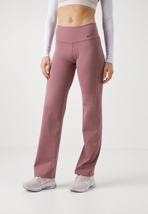 Persona con pantalones de pierna recta de talle alto en color malva, zapatillas Nike rosas y blancas, y un top blanco corto de manga larga sobre un fondo liso.