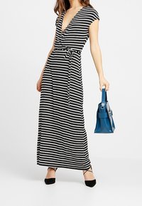 Černobíle pruhované zavinovací šaty s krátkými rukávy, hlubokým V výstřihem a kravaty. V kombinaci s modrou kabelkou a černými balerínkami.