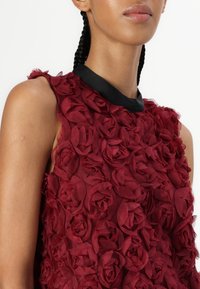 Rode bloemenjurk met gelaagde stofrozen, een mouwloos ontwerp en een contrasterende zwarte halslijn. Zachte textuur met ingewikkelde details.