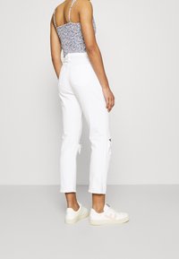 Jeans blancos de tiro alto con detalles desgastados; combinados con una camiseta sin mangas de estampado floral y zapatillas blancas con acentos en rosa.