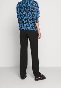 Black trousers paired with a black and blue floral patterned blouse featuring puffed sleeves and a scalloped hem. Flat black shoes are worn.