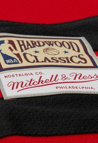 Roter Stoffpatch mit dem Aufdruck "Hardwood Classics" und NBA-Logo. Akzente umfassen einen schwarzen Rand und den Text "Mitchell & Ness" in rot.