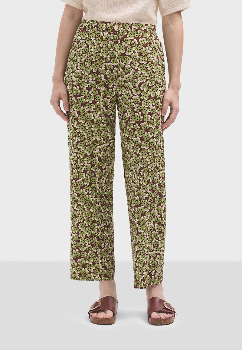 Des pantalons à motifs verts et bruns affichent une taille haute, des jambes droites et une fermeture à bouton. Portés avec des sandales brunes.