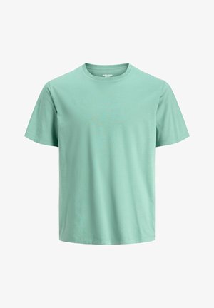 Sort lynlåstrøje over en lysegrøn t-shirt, kombineret med viddebenede blå jeans. Skoene er hvide med sorte såler. Simpelt, afslappet outfit.