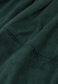 Tissu en suède vert foncé avec une texture douce, présentant des coutures visibles et une surface lisse. Apparence pliée et légèrement froissée.