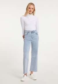 Blugi de culoare albastru deschis, cu talie înaltă, design drept, tiv dus și două buzunare frontale, asortați cu un top alb cu mânecă lungă.