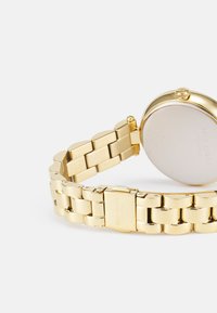 Gold-tone metal wristwatch with a linked bracelet, rounded case, and a polished back. Features a simple, clean design with a clasp closure.
