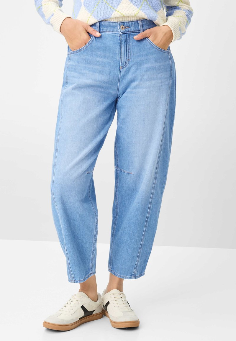 Lichtblauwe denim jeans met hoge taille en een ontspannen pasvorm, voorzien van voorzakken en nette zomen. Gecombineerd met beige en zwarte sneakers.