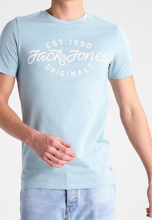 T-shirt en coton bleu clair avec manches courtes. Sur le devant, texte blanc « EST 1990 Jack & Jones Originals ». Texture lisse, coupe décontractée.