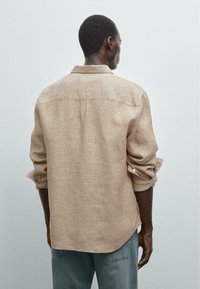 Beige linen shirt with long sleeves, rolled up at the cuffs, and a back yoke design. Shirt features a relaxed fit and subtle texture.