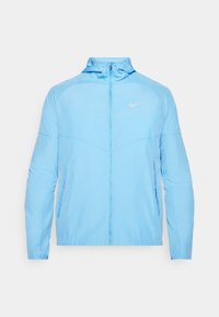 Chaqueta Nike de color azul claro con cremallera completa, cuello alto y dos bolsillos laterales. Presenta un tejido suave y liviano, además de un sutil logo en el pecho.