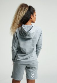 Felpa grigia con una vestibilità morbida, dotata di cappuccio con coulisse e maniche raglan, abbinata a pantaloni corti grigi coordinati e dettagli bianchi a zigzag.