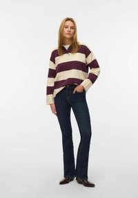 Gestreepte sweatshirt in crème en donkerpaars, met een kraag en lange mouwen, gecombineerd met donkerblauwe flare jeans en bruine enkellaarsjes.