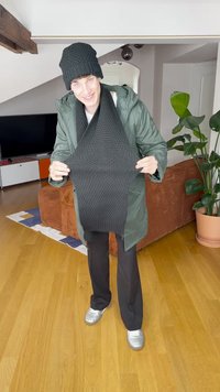 Fular tricotat negru ținut sus, cu un model texturat. Purtați împreună cu o căciulă tricotată neagră asortată și o jachetă verde, completate de pantaloni negri.