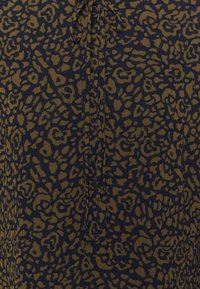 Marinblå tyg med leopardmönster i mörk oliv. Har en knytning vid halslinningen, med en mjuk textur och knappslå.