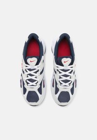 Vita och marinblåa idrottsskor med ovandel i mesh, röda accenter och vita snören. Har en vadderad krage och en signaturlogo på tungan.