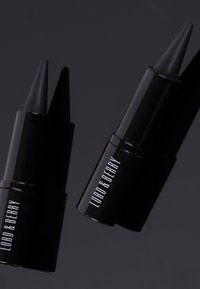 Deux crayons eye-liner noirs Lord & Berry avec des pointes effilées sur un fond sombre.