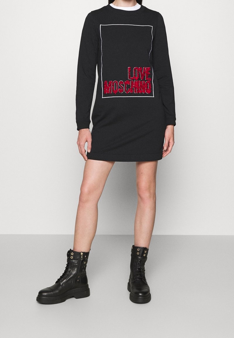Black long-sleeve dress with a rectangular white outline and red "LOVE MOSCHINO" text. Paired with black lace-up combat boots.
