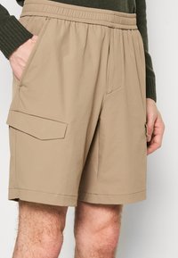 Béžové šortky vyrobené z ľahkého materiálu, s elastickým pásom, bočnými vreckami a cargo vreckom s detailom klopy.