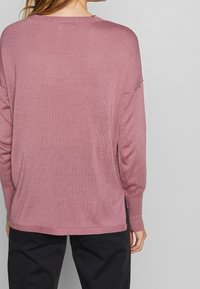 Różowy sweter dziewiarski o luźnym kroju, z długimi rękawami, rozcięciami po bokach oraz ściągaczami przy mankietach i hemie. Gładka tekstura z lekkim, oddychającym materiałem.