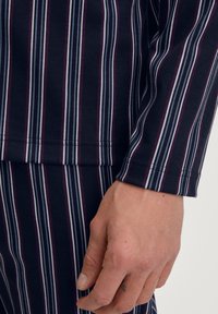 Marineblauwe long sleeve shirt met verticale strepen in paars, wit en lichtblauw. Heeft een zachte textuur en een nauwsluitend manchetontwerp.