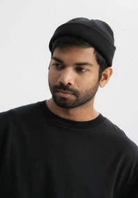 Zwarte beanie muts van ribgebreide stof, met een nauwsluitend ontwerp. Draag hem met een zwart crewneck t-shirt, dat een textuur geeft.