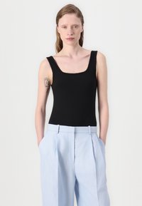 Musta ribattu bodysuit, jossa on neliönmuotoinen pääntie, yhdistettynä vaaleansinihin korkeavyötäröisiin housuihin, joissa on etutaskut ja sivutaskut.