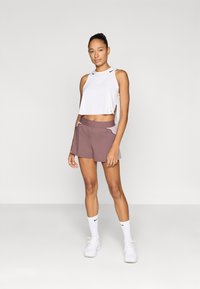 Camiseta sin mangas blanca recortada con aberturas laterales, combinada con pantalones cortos deportivos de color púrpura claro que tienen bolsillos y una cinturilla contrastante.