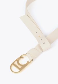 Beżowy skórzany pasek z szerokim paskiem i złotym metalowym zapięciem z wyciętym wzorem. Zawiera otwory do regulacji rozmiaru.