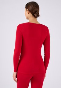 Maglietta rossa a maniche lunghe realizzata in tessuto elastico con scollatura a barca. Presenta un design aderente che si adatta al corpo, con una texture liscia.