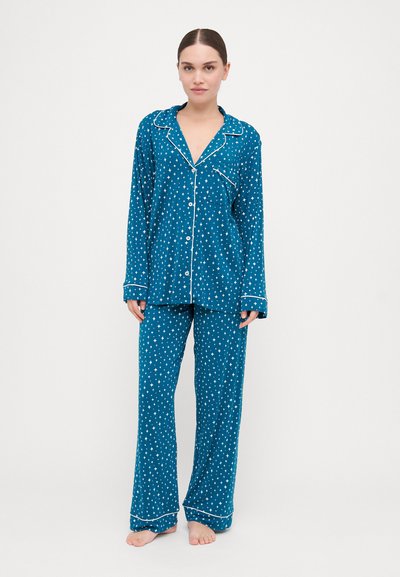 Conjunto de pijama em turquesa feito de tecido suave, com padrões de estrelas brancas e um acabamento em branco contrastante. Inclui uma camisa de botão e calças.