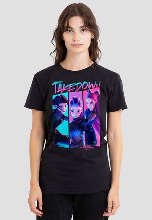Young woman wearing black T-shirt with colorful graphic of three animated female characters and the text "TAKEDOWN" and "K-POP DEMON HUNTERS".