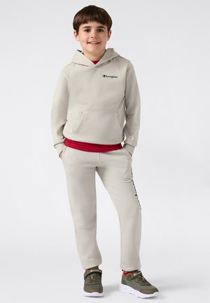 Sudadera gris claro con bolsillo frontal y logo en azul marino, combinada con pantalones de chándal a juego, que presentan acentos en logo negro y zapatillas en verde oliva.