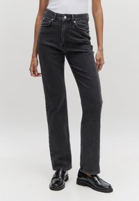 Zwarte high-waisted jeans met een rechte pijp, voorzien van vijf zakken, een knoopgulp en een klassieke denim textuur. Glanzende zwarte loafers completeren de look.