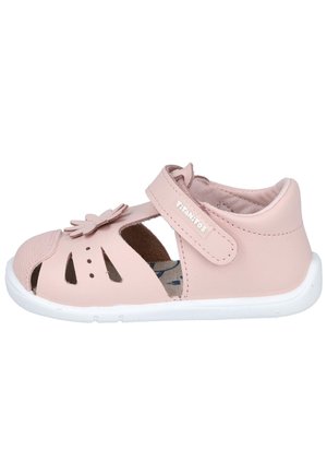 Sandalia rosa para niña pequeña con punta cerrada, ventilación recortada, decoración de flor en la correa y suela de goma blanca sobre fondo blanco.