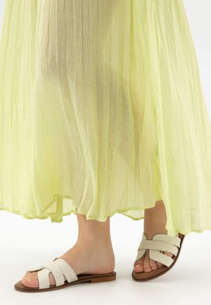 Sandali bianchi con ampie strap incrociate, abbinati a una lunga gonna maxi di un leggero giallo chiaro con un bordo arricciato.