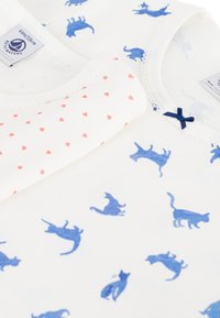 Δύο βαμβακερές μπλούζες: η μία εκρού με μπλε σιλουέτες γάτας, η άλλη εκρού με μικρές κόκκινες καρδιές. Διαθέτει μπλε φιόγκο και λεπτομέρεια δαντέλας στο ντεκολτέ.