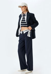 Marintröja i oversized modell över en randig crop top, vida marinblå byxor och en ljus hatt. Synliga randiga detaljer på midjebandet.