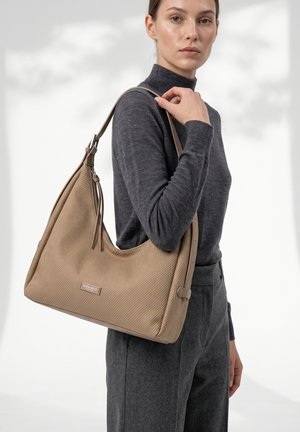 Donna con abito grigio porta una grande borsa beige a tracolla testurizzata con cerniera e tracolla regolabile.