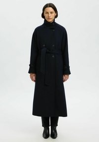 Cappotto lungo in lana navy con chiusura a doppia fila di bottoni, colletto alto, vita con cintura e maniche lunghe. Texture liscia, design minimale.